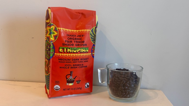 bag of Trader Joe's coffee sitting next to a glass mug of coffee beans on a counter