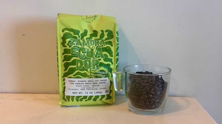 bag of Trader Joe's coffee sitting next to a glass mug of coffee beans on a counter
