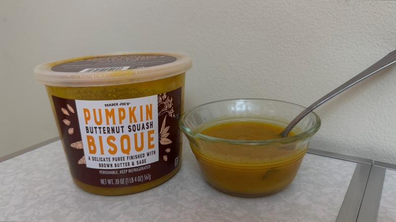 A tub and a small bowl of Trader Joe's Pumpkin Butternut Squash Bisque on a table with a spoon in it
