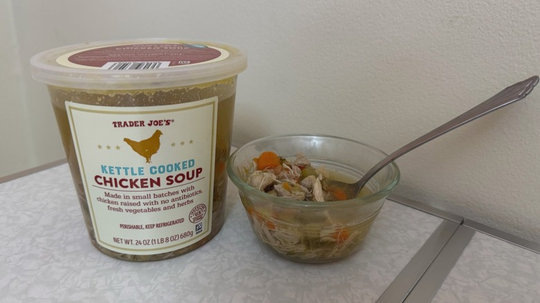 A tub and a small bowl of Trader Joe's Kettle Cooked Chicken Soup on table with a spoon in it