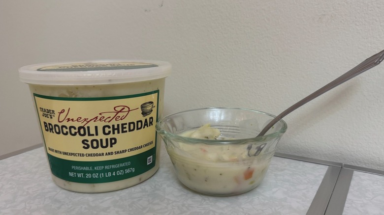 A tub and a small bowl of Trader Joe's Unexpected Broccoli Cheddar Soup with a spoon in it