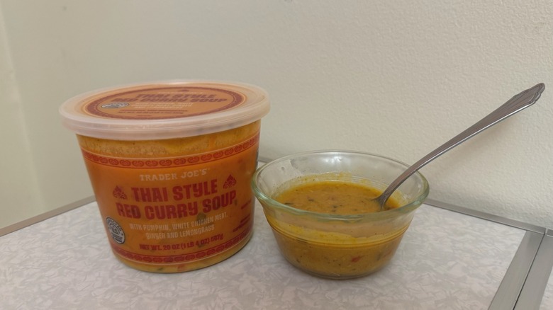 A tub and a small bowl of Trader Joe's Thai Style Red Curry Soup with a spoon in it