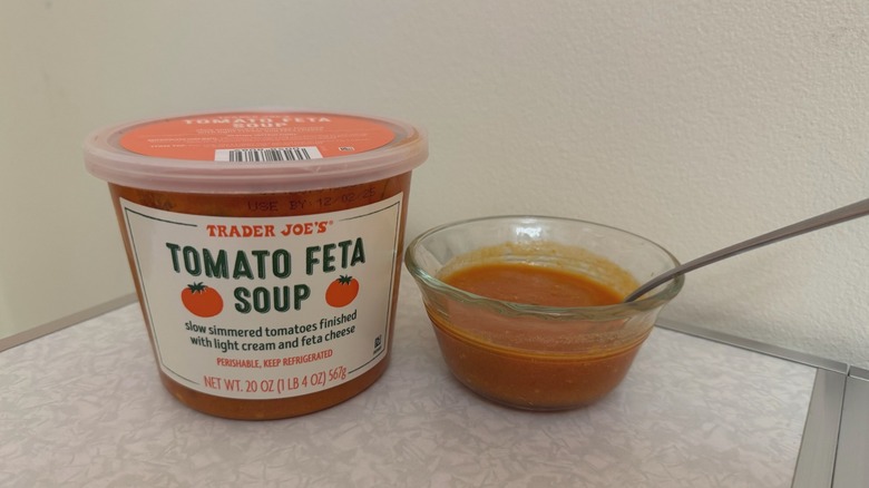 A tub and a small glass bowl of Trader Joe's Tomato Feta Soup with a spoon in it
