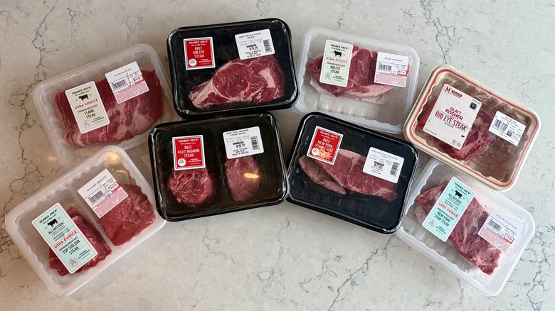 A lineup of eight packaged raw steaks from Trader Joe's