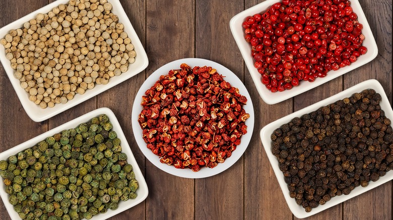 Types of peppercorns in bowls on brown surface