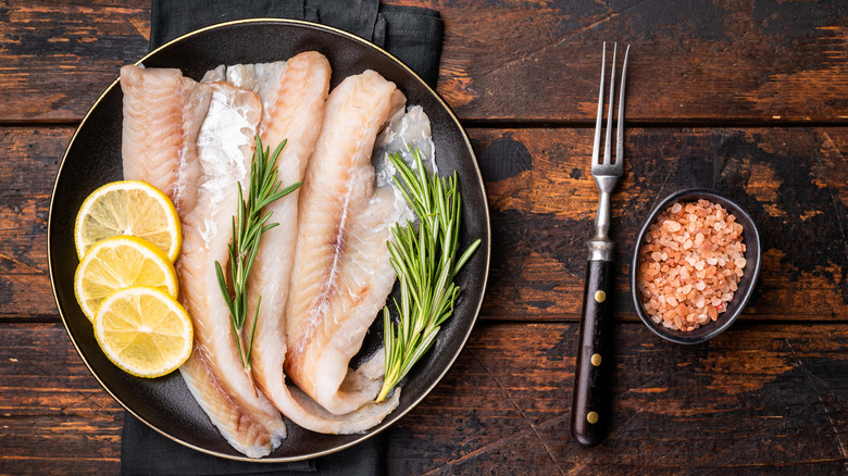 raw haddock with lemons and herbs on cutting board