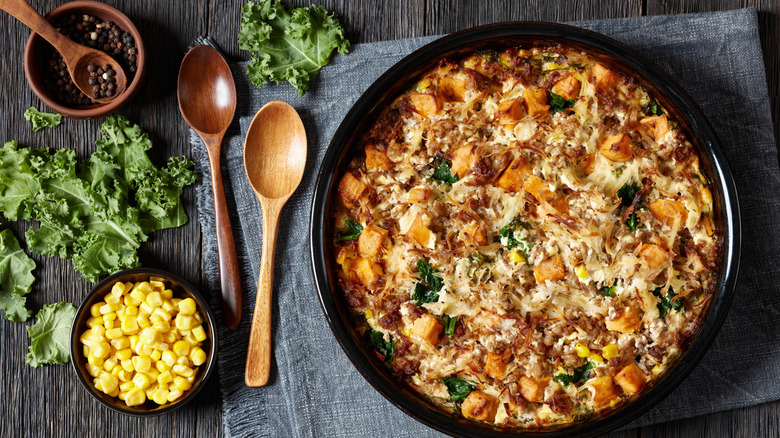 Breakfast casserole in black dish, with vegetables and wooden utensils alongside