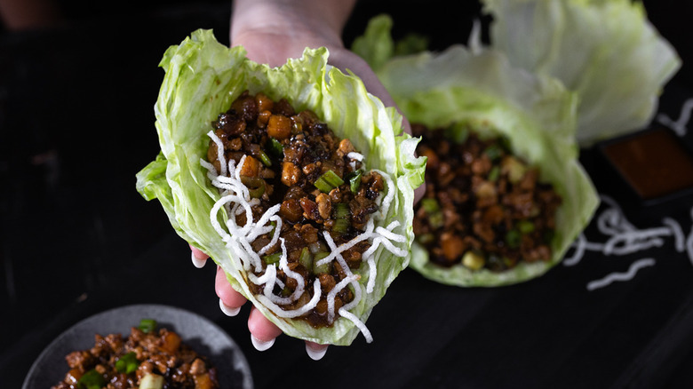 Hand holding leaf of lettuce filled with meat and veggie mixture