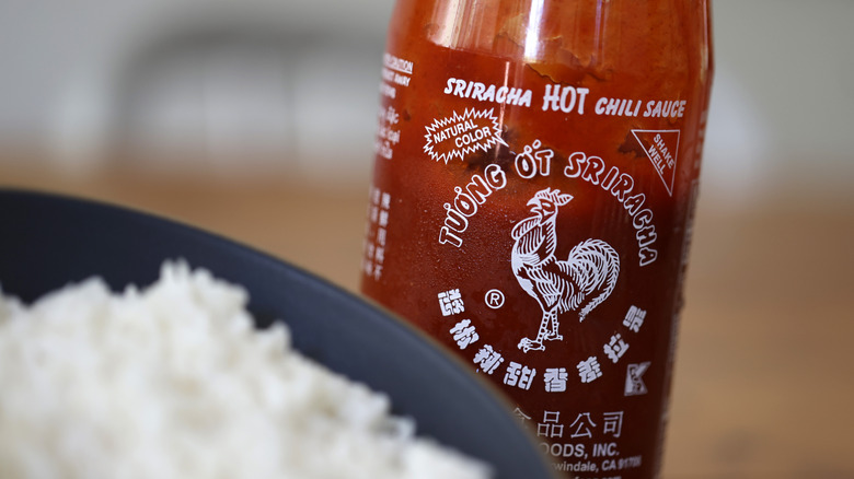 Close-up of Sriracha bottle with blurred rice in front