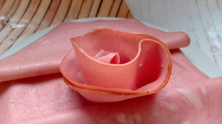 Sliced meat rolled to look like a rose, sitting on other slices of meat on a white plate