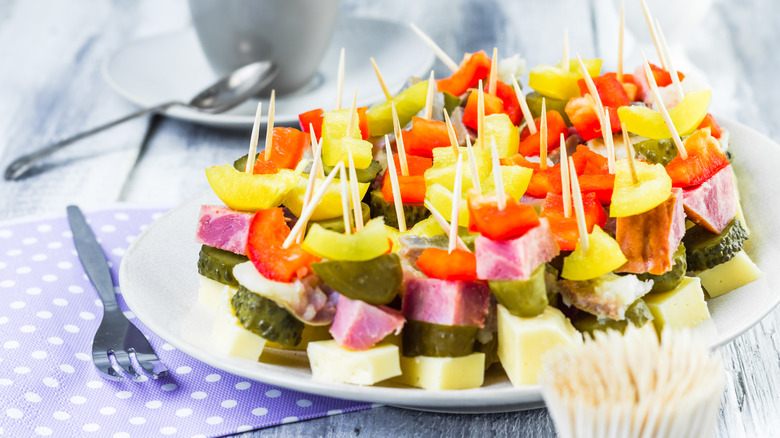 Canapes made with bologna, cheese, and vegetables held together with toothpicks on a white plate