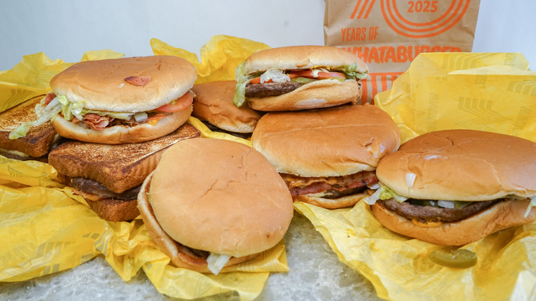 Scattered pile of burgers on wrappers with brown paper Whataburger bag in background