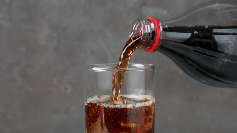 A bottle of cola being poured into a glass of ice