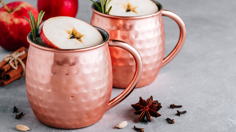 two apple cider mules with apple slice and rosemary served in a copper mug