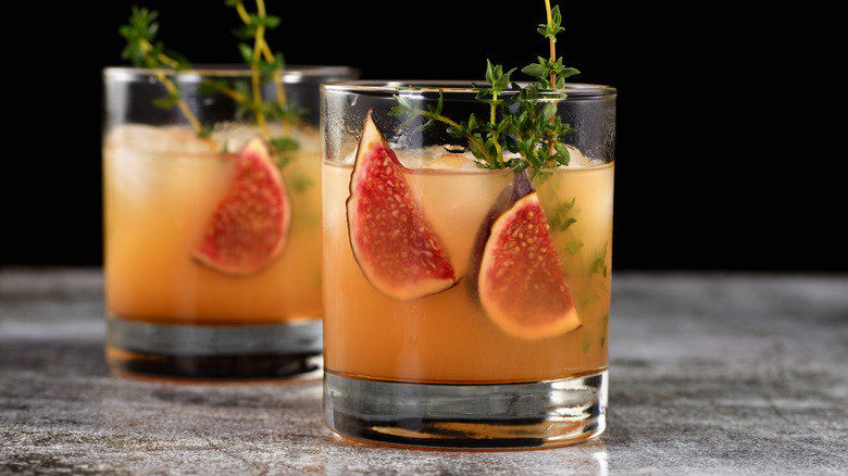 two fig and bourbon cocktails behind a black background