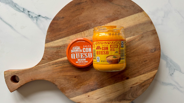 Jar of Salsa Con Queso on round, wooden cutting board