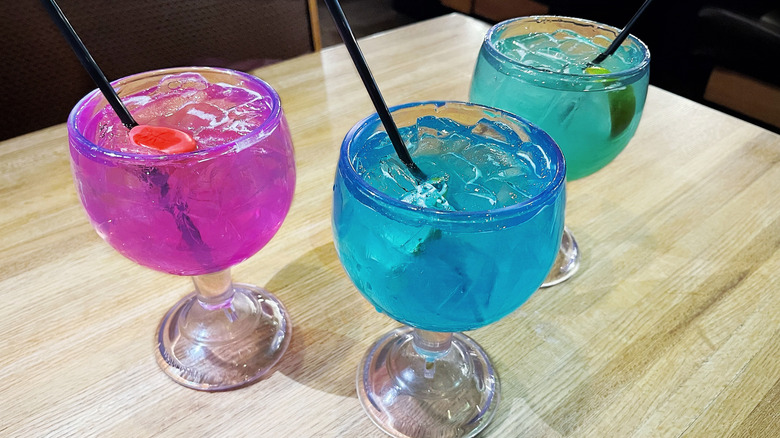 Three brightly colored Applebee's cocktails on a table in mucho goblets