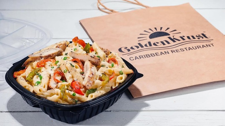 A bowl of jerk chicken pasta in front of a takeout brown bag from Golden Krust