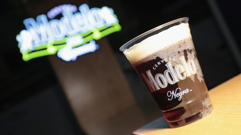 An angled shot showing a frothy glass of Negra Modelo beer in front of a blurry Modelo neon sign