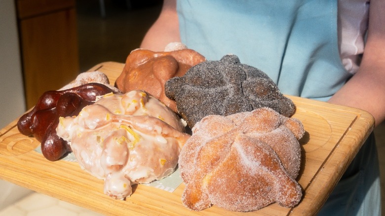 A person holding a cutting board with different pan de muertos from Consuelo Pan de Madre.