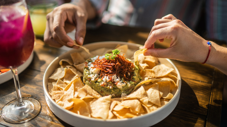 People scooping chips into a dip at a party