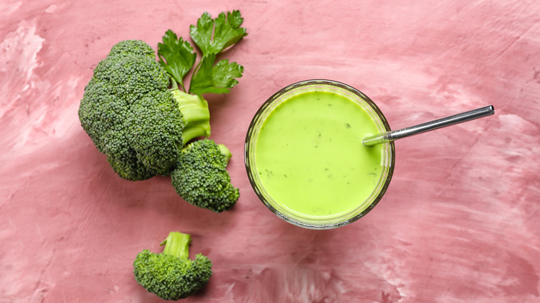 glass of broccoli juice and fresh broccoli on a pink backdrop