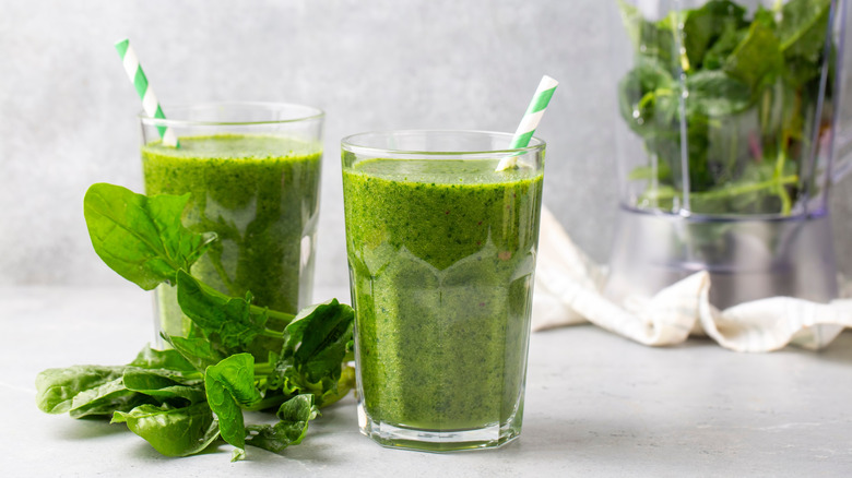 two glasses of green juice with some spinach on table