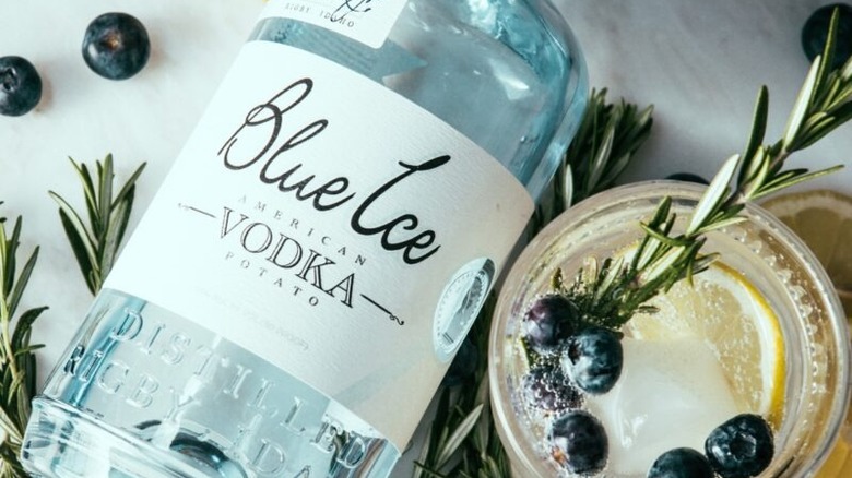 A bottle of Blue Ice American vodka next to a cocktail garnished with blueberries and rosemary