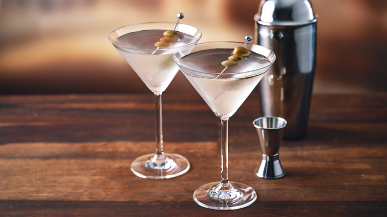 Two chilled martini glasses sit on a wooden surface with an olive garnish