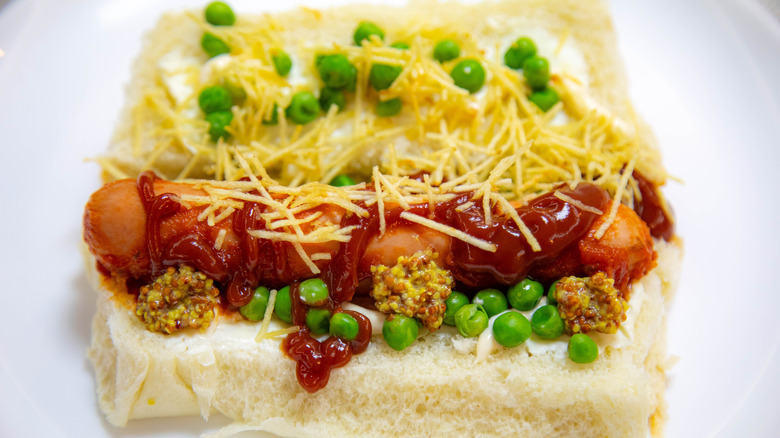 A Brazilian hot dog on soft white bread featuring toppings including peas, potato straws, and mashed potatoes