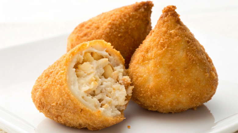 Three coxinga in front of a white background, with one exhibiting a bite mark that exposes its filling