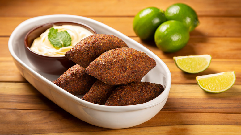 Quibe served with a dipping sauce and limes