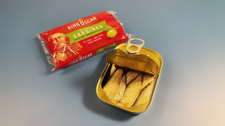 King Oscar sardines with the lid partially opened next to the paper packaging