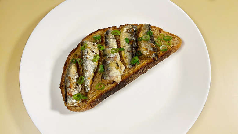 A piece of toast with different types of sardines arranged on it and a green onion garnish