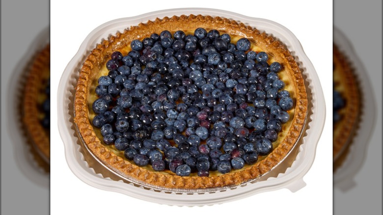 Blueberry-topped custard pie  with a golden crust in an aluminum pie pan on a white background