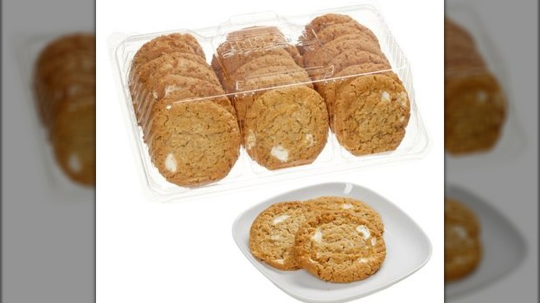 Package of Marshmallow Crispy Cookies in the background with three of the cookies on a white plate in foreground.