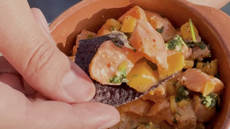 Close-up of a hand holding a tortilla chip topped with Costco's salmon mango ceviche