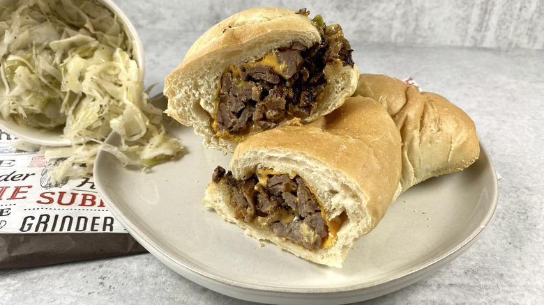 The Loaded Cheesesteak Bomb from Primanti Brothers cut in half on a plate next to a bowl of coleslaw.