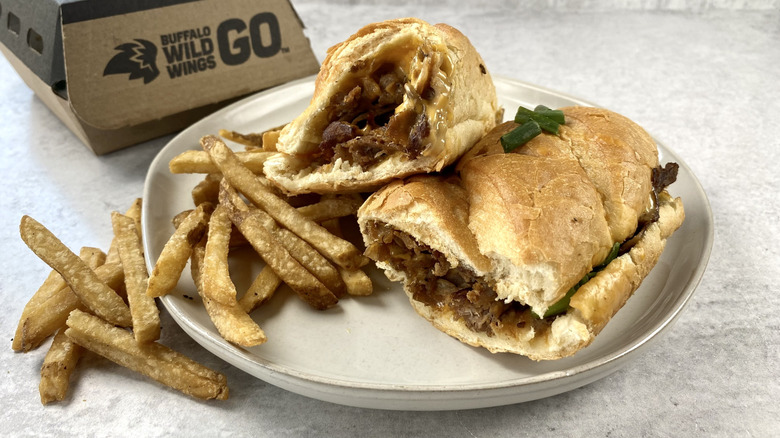 The Beer Cheese Cheesesteak from Buffalo Wild Wings cut in half on a plate next to french fries.