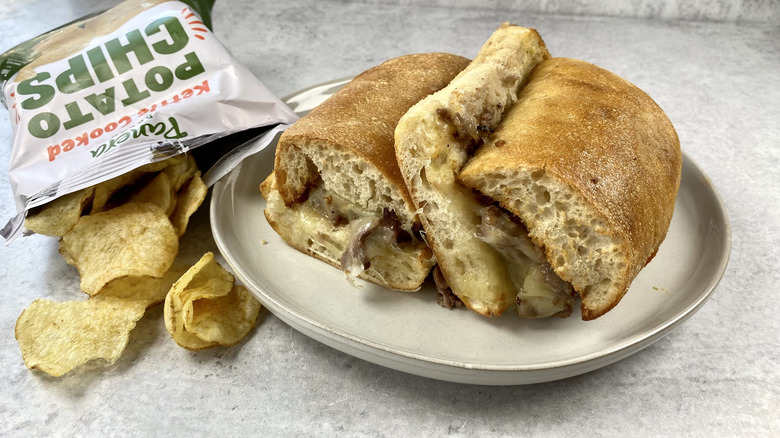 Panera Bread's Ciabatta Cheesesteak on a plate next to a bag of potato chips.