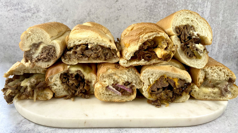 Two rows of stacked cheesesteaks on a marble cutting board.