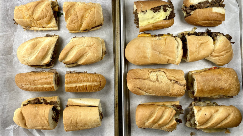 Rows of cheesesteaks cut in half on parchment paper.