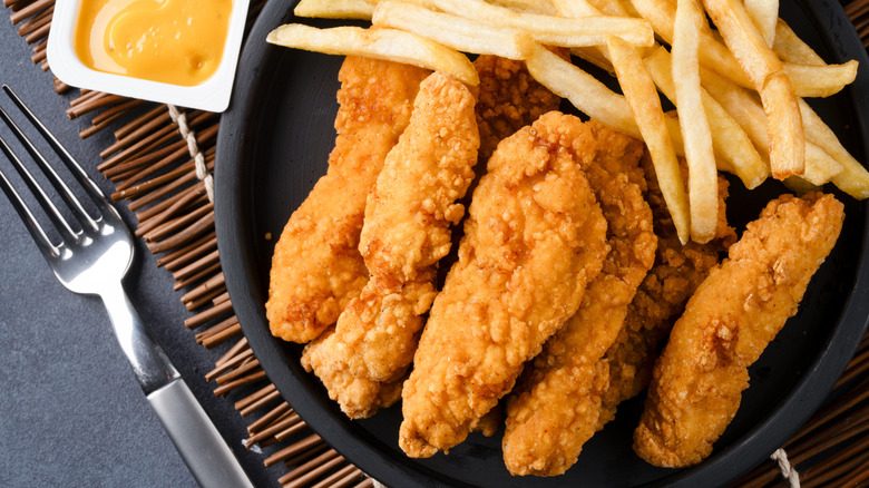 A plate of chicken tenders with fries and dipping sauce