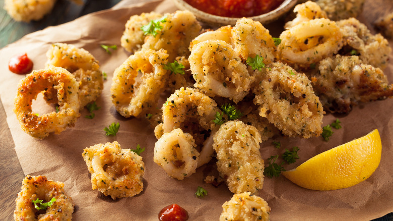 Pieces of fried calamari on brown paper with a lemon wedge