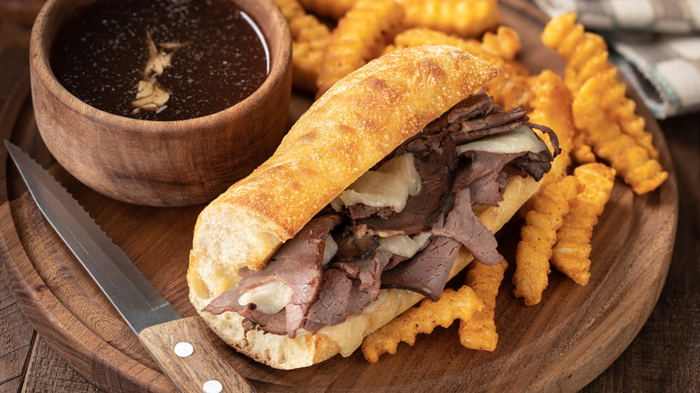 A French dip sandwich with fries on a wooden plate