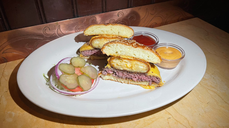 The cross section of the Macaroni and Cheese Burger with pickles, onion, and tomato on the side