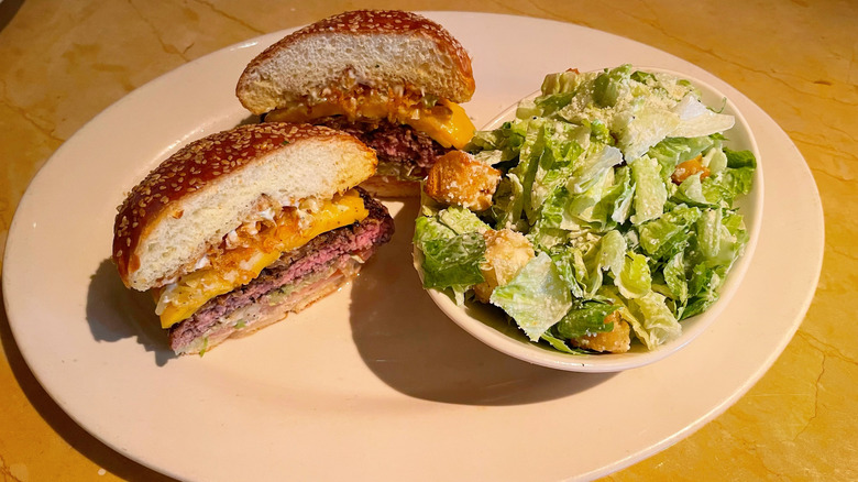 The cross section of the Americana Cheeseburger with a side bowl of Caesar salad