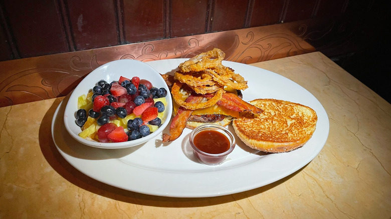 A bowl of fruit next to the Smokehouse BBQ Burger piled high with crispy onion strings