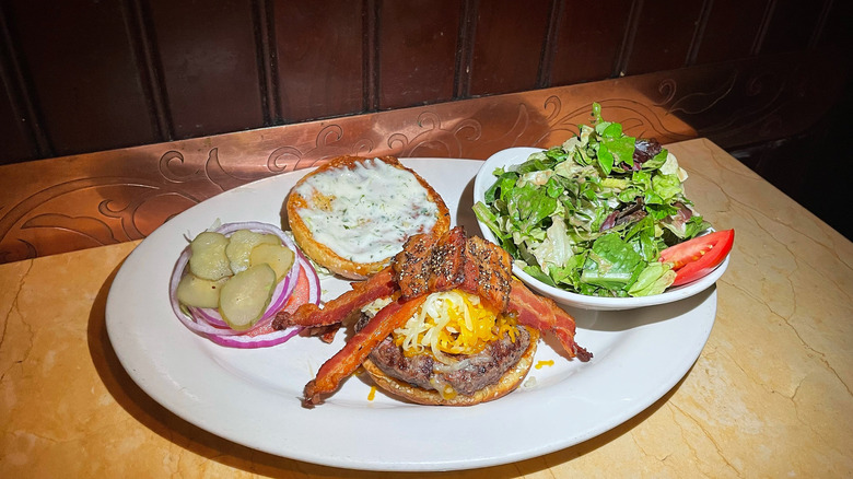 The Bacon-Bacon Cheeseburger split open with onions, pickles, and a bowl of salad on the side