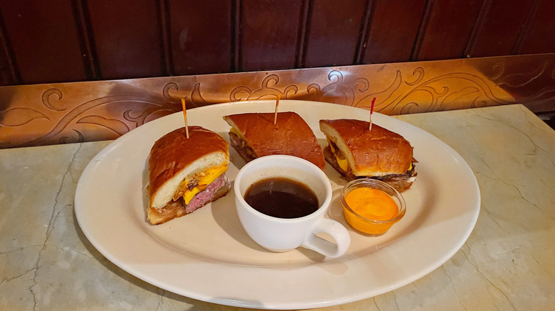 The French Dip Cheeseburger split into three pieces with cup of au jus and a side of sriracha mayo